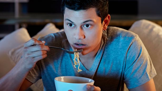 Young-man-eating-noodles-and-watching-tv