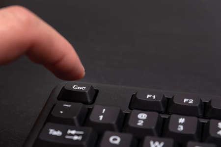 170038528-finger-reaches-for-the-esc-button-black-keyboard-escape-key